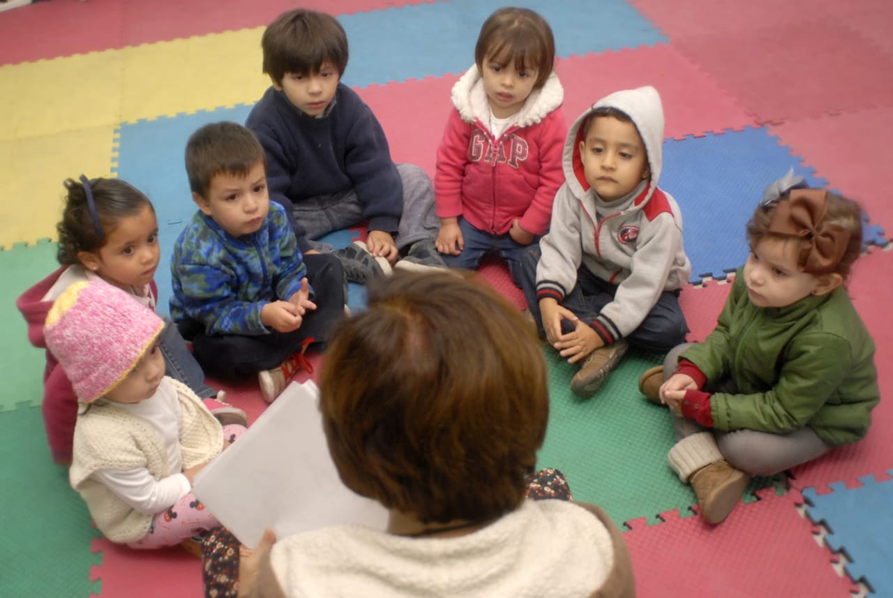 Niñas y niños pequeños sentados en un tapete con su maestra
