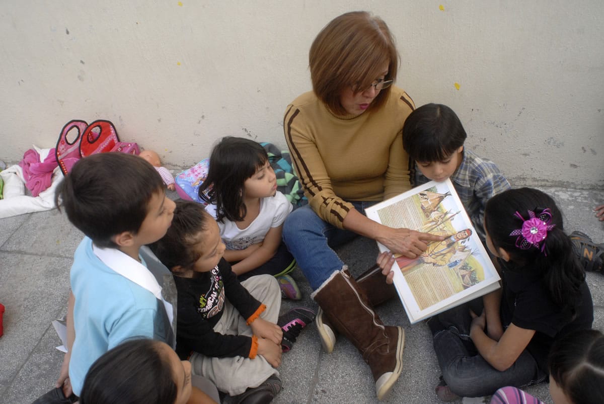 Maestra lee un libro a niñas y niños sentados en el piso