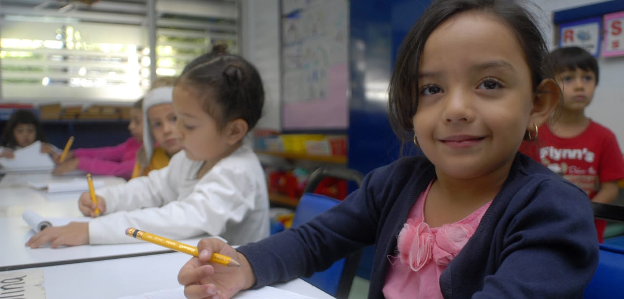 Niña de preescolar sonríe mientras escribe con su lápiz amarillo