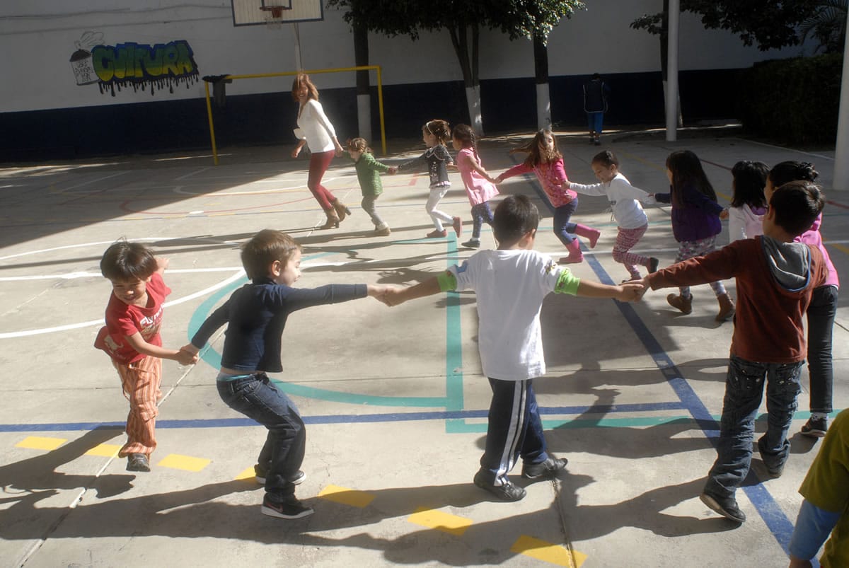 Niñas y niños forman una ronda de la mano en el patio